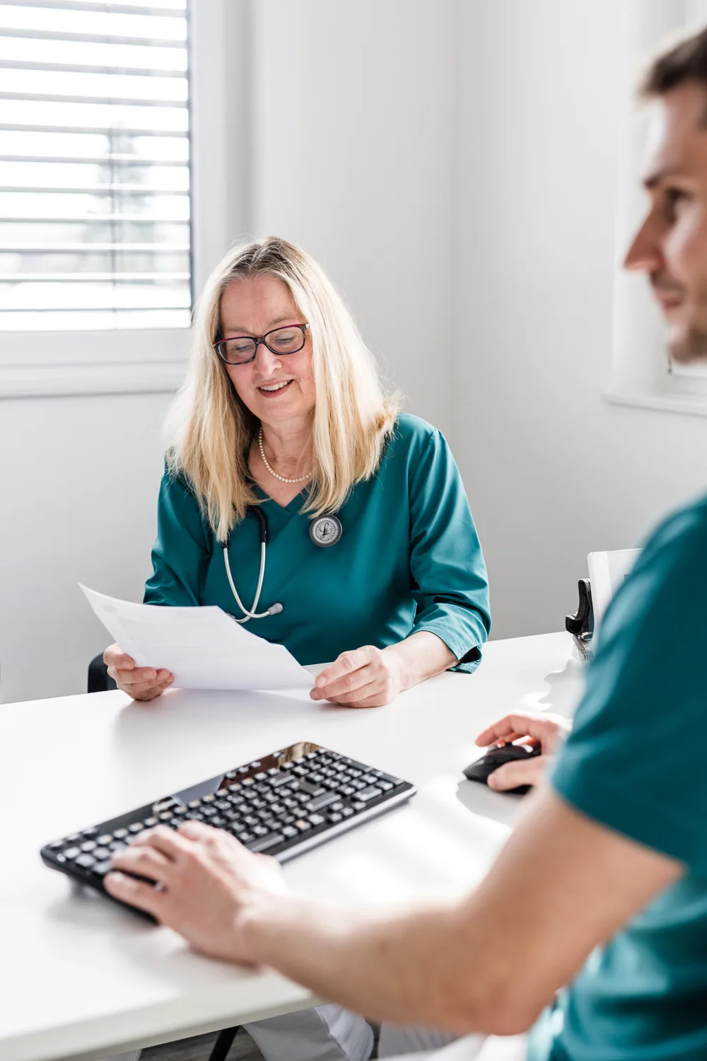 Ärztin am Schreibtisch im Gespräch mit einem Patienten